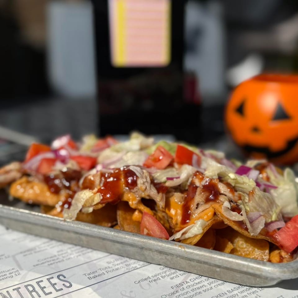 GB's Pub & Grub's loaded nachos with BBQ sauce, lettuce, tomatoes, and onions, next to a Halloween pumpkin.