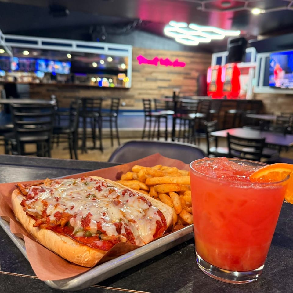 A cheesy sub sandwich with fries and a red cocktail with an orange slice at GB's Pub & Grub.