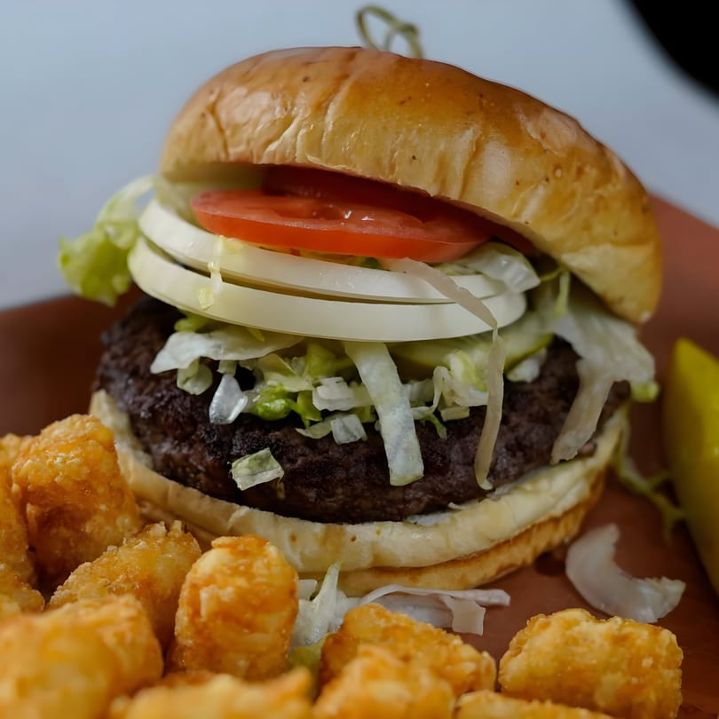 A GB's Pub & Grub burger with lettuce, tomato, and onion, served with tater tots.