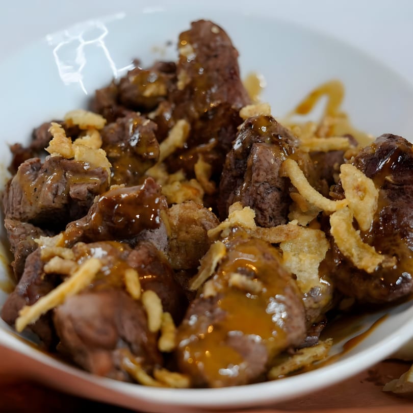 Close-up of GB's Pub & Grub's beef tips with gravy and crispy fried onions in a white bowl.