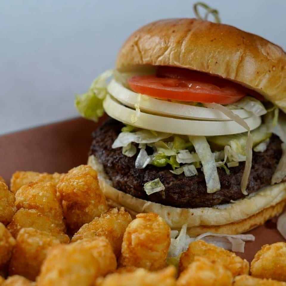 A GB's Pub & Grub burger with lettuce, onion, and tomato, served with crispy tater tots.